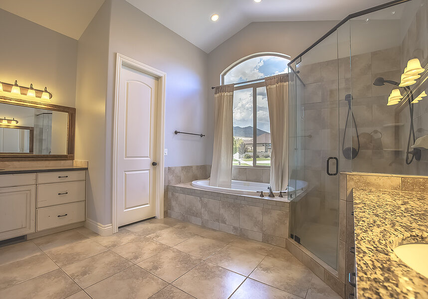 Oval bathtub in front of the arched window of a bathroom with tiled floor
